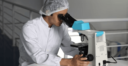 Technician examining a sample under a microscope in the test lab
