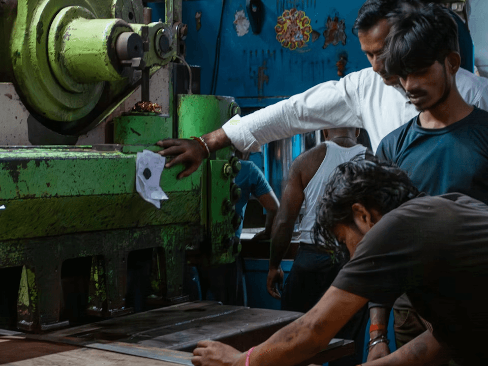 Operators working a compression press on the Nashik production floor